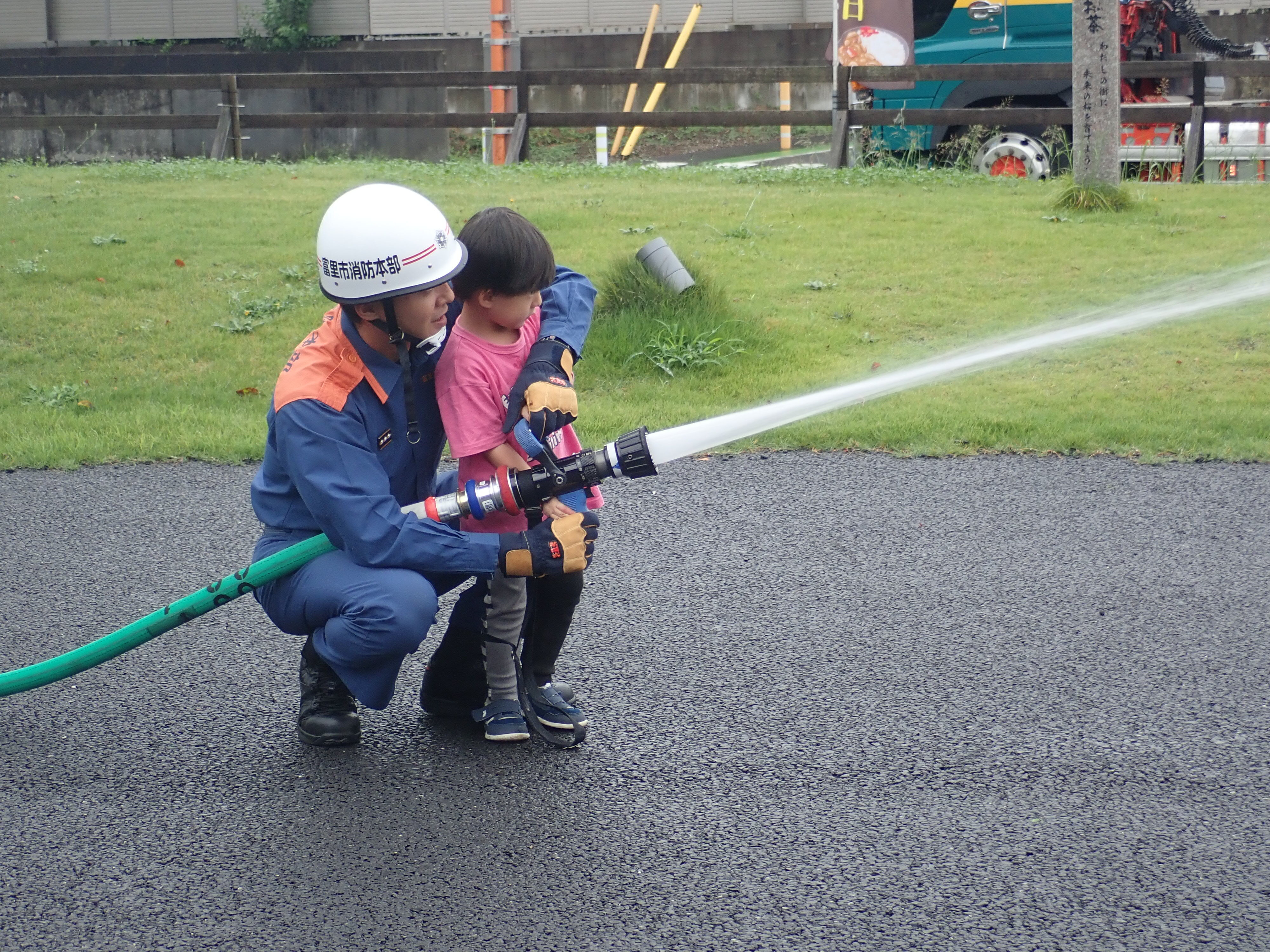 消防隊員と参加者の子どもが消防車から放水している様子