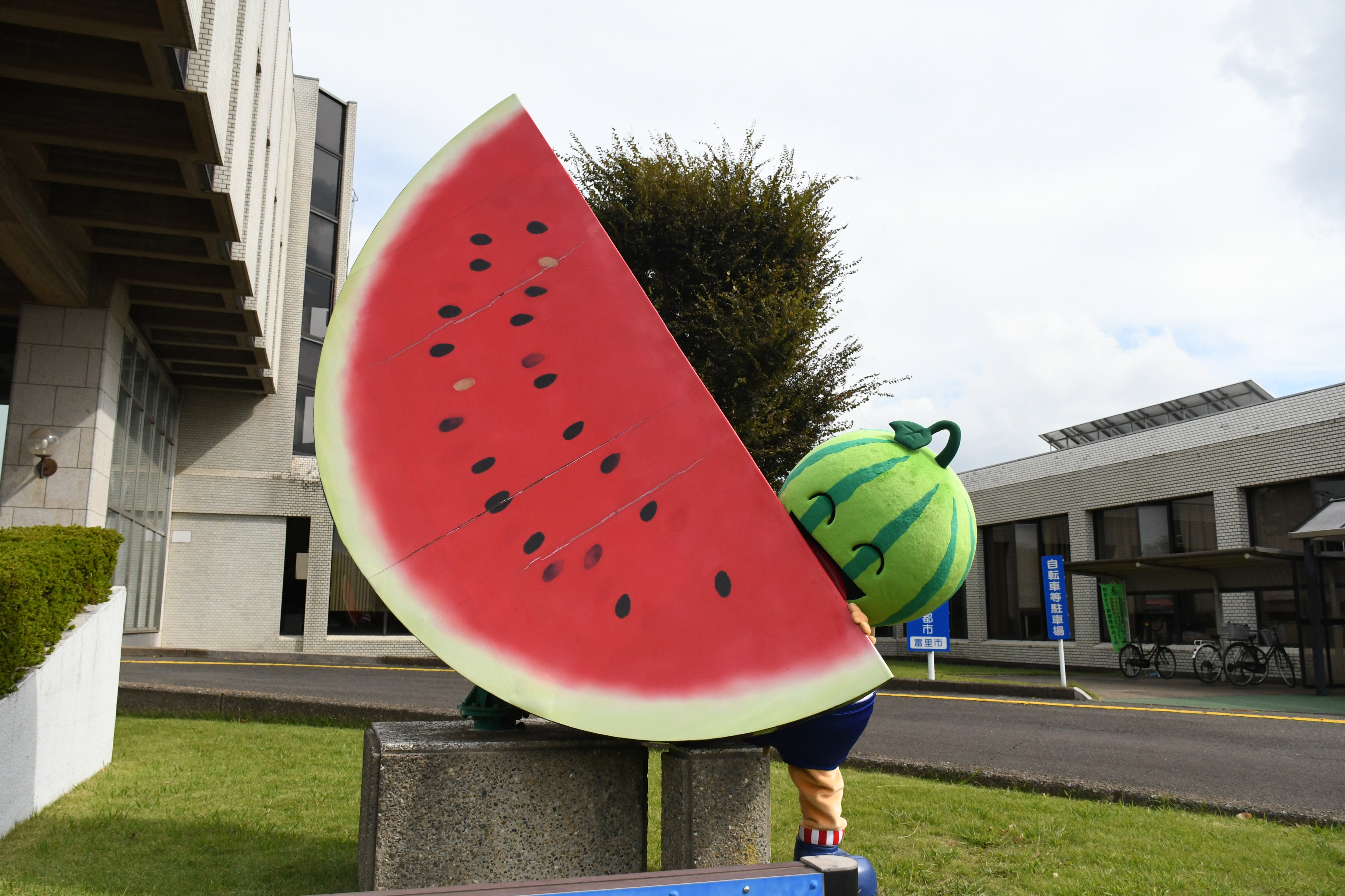 市公式マスコットキャラクター「とみちゃん」が富里市役所正面玄関前に設置しているスイカのモニュメントにて記念撮影している様子